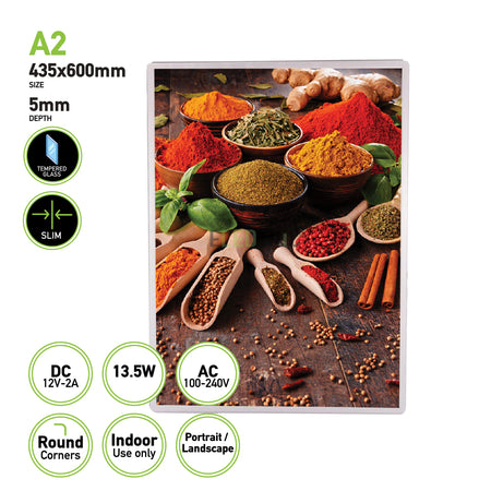 The Eledtric LED Light Box A2 Silver Slim Advertising Wall Mounted Display features a framed image showcasing spices in bowls and wooden spoons on a wooden surface, highlighted by vibrant powders and herbs. The display measures 435x600mm with a depth of 5mm and is ideal for indoor use. This frame can be mounted in both portrait and landscape orientations to beautifully illuminate the scene.